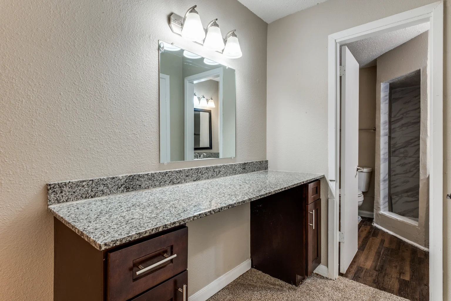 A vanity nook in dark cherry, lit from above, opening to the bathroom beyond.