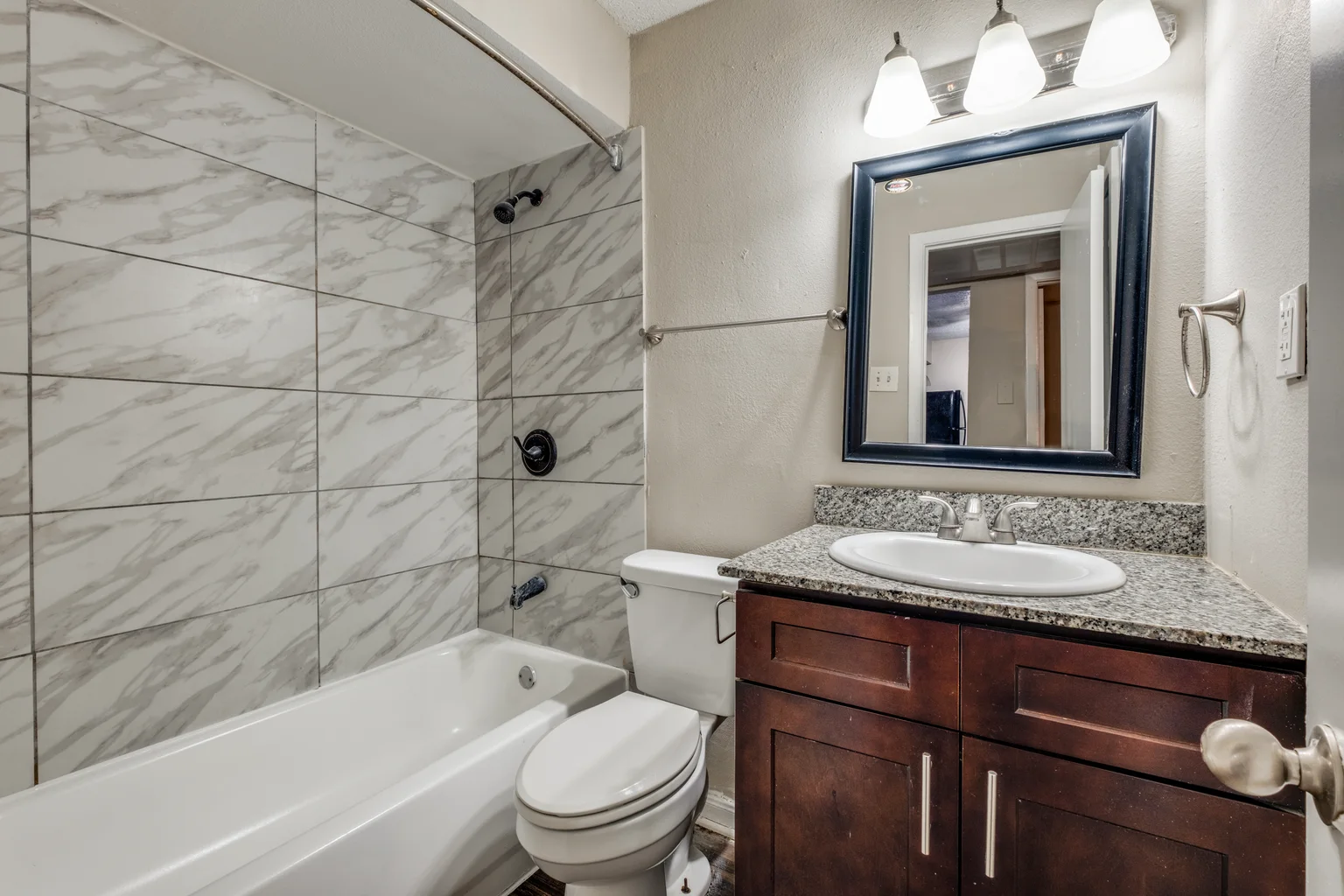 A bathroom with a marble look tiled tub surround and a dark vanity beside it.