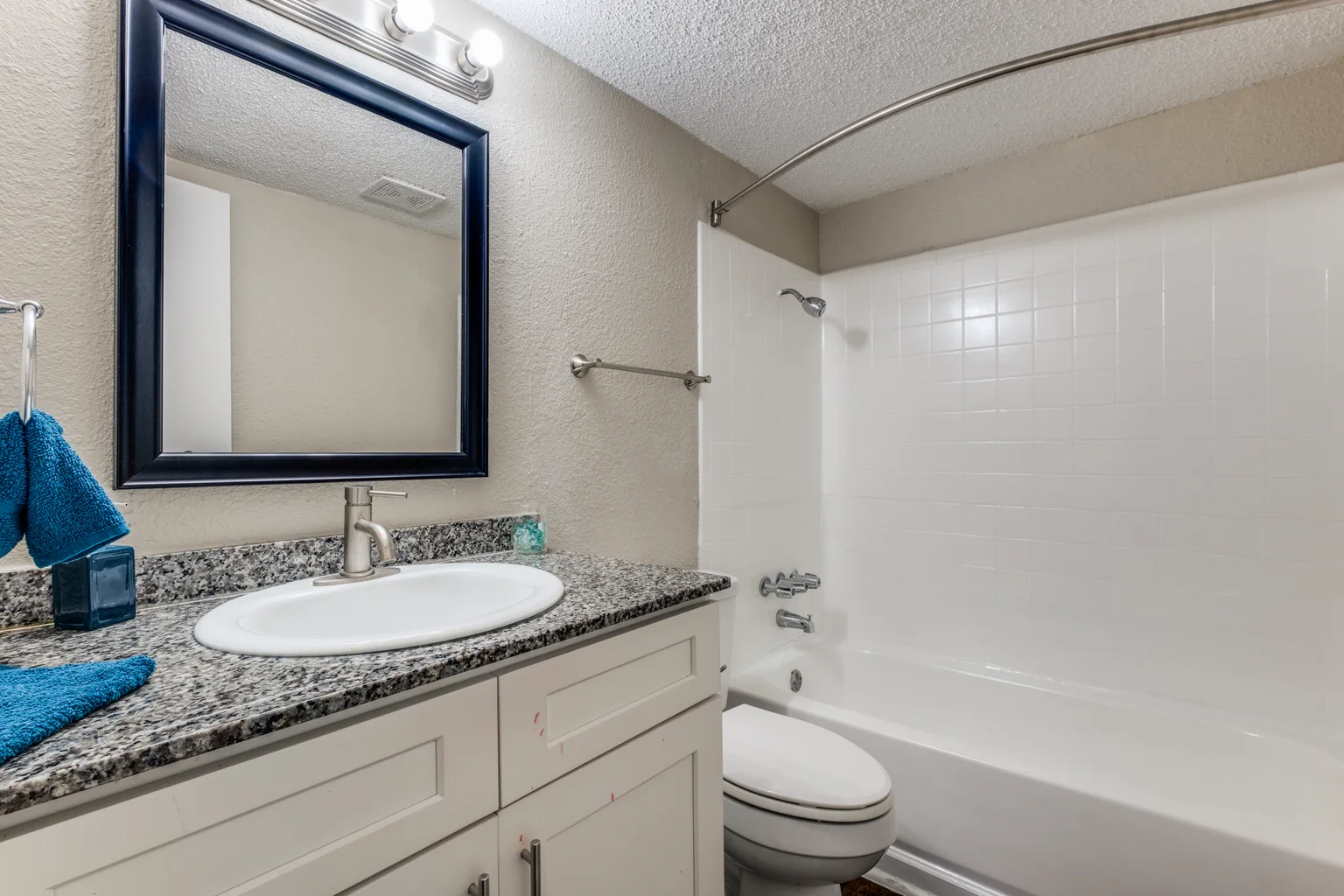 A bathroom with a white vanity, a speckled counter and the tub and shower beyond.