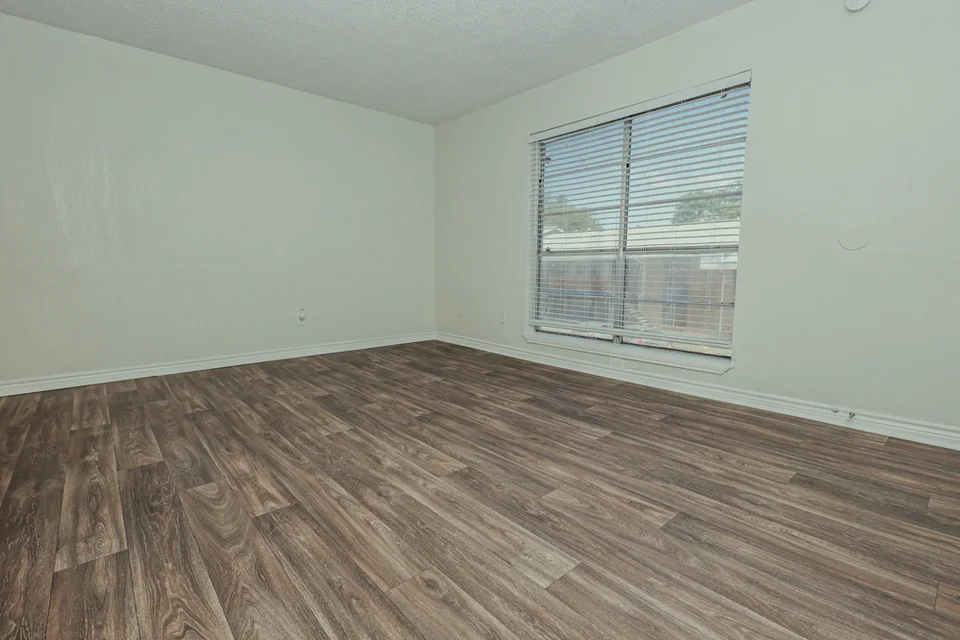 A bedroom with a large window and wood look plank flooring.
