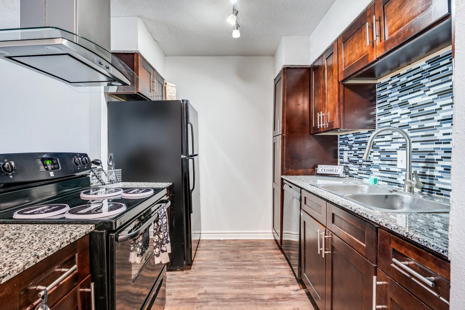 Dark cherry cabinets and a glass mosaic backsplash, with the range and the sink below.