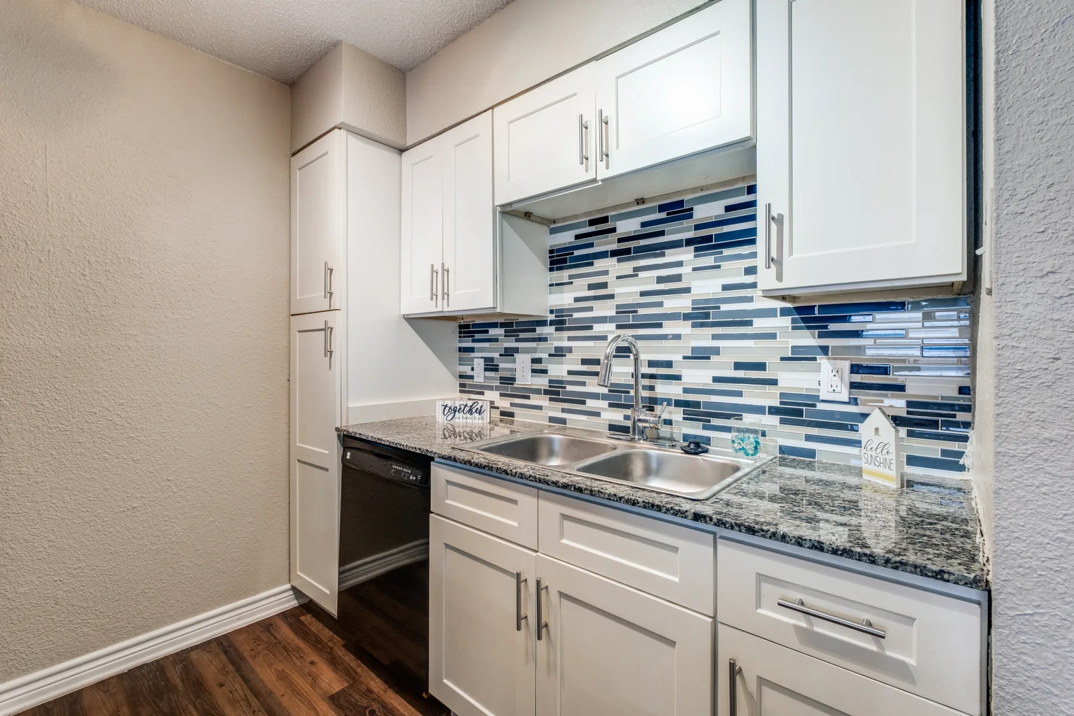 A kitchen with white cabinets and a blue and grey mosaic backsplash.