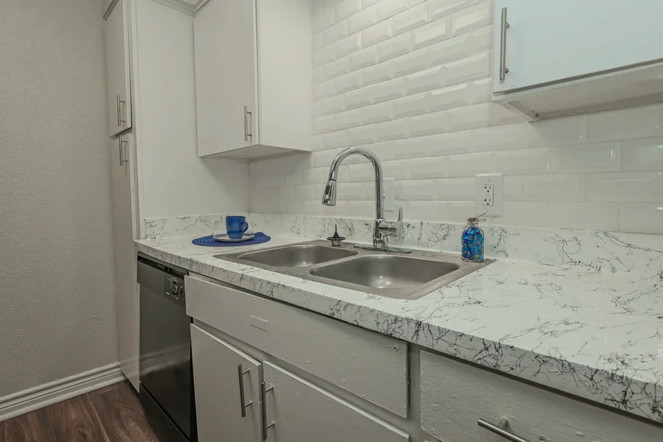A kitchen with white cabinets, a marble look quartz counter and the refrigerator beside the range.