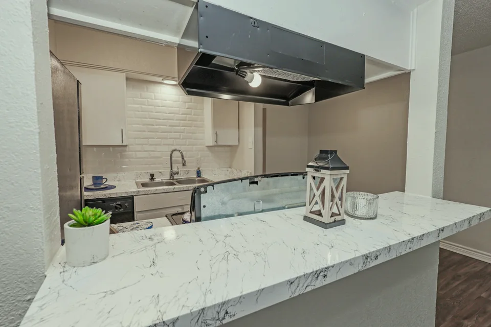A kitchen with white cabinets, white subway tile and a counter through to the next room.