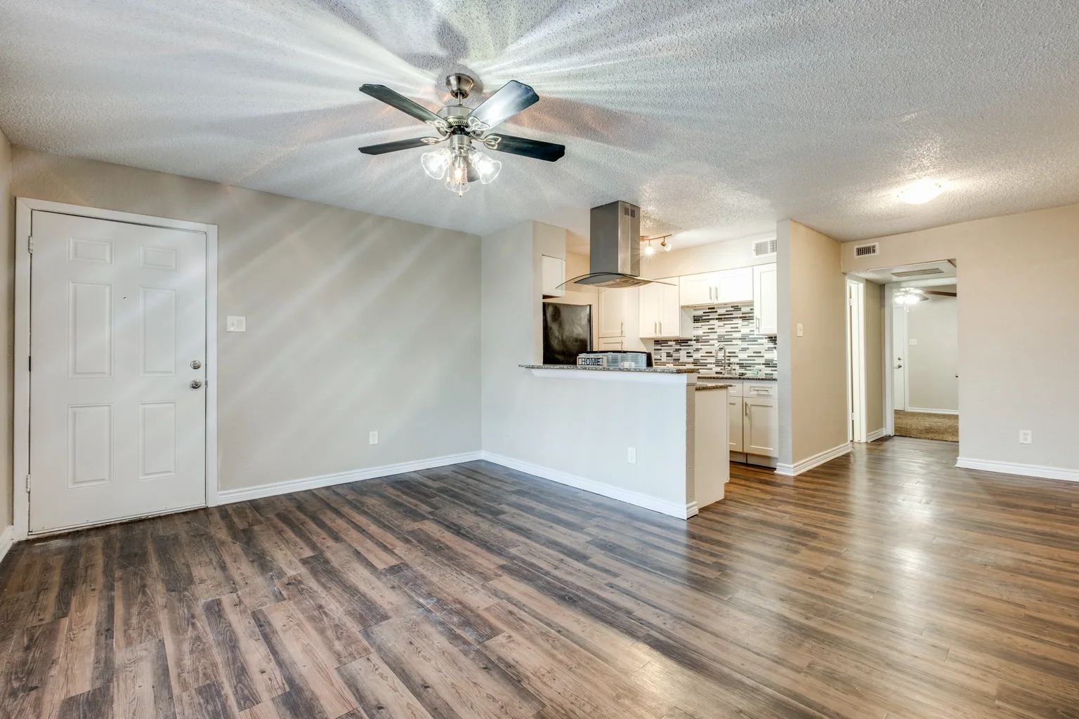 A living room with the kitchen and its extractor hood visible across the room.