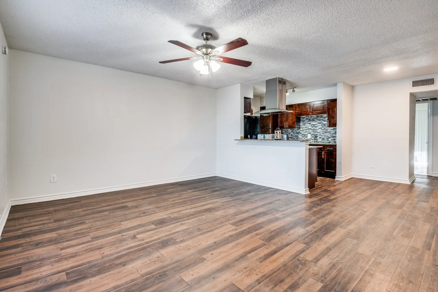 A living and dining room open through to the kitchen, ceiling fan and track lights above.