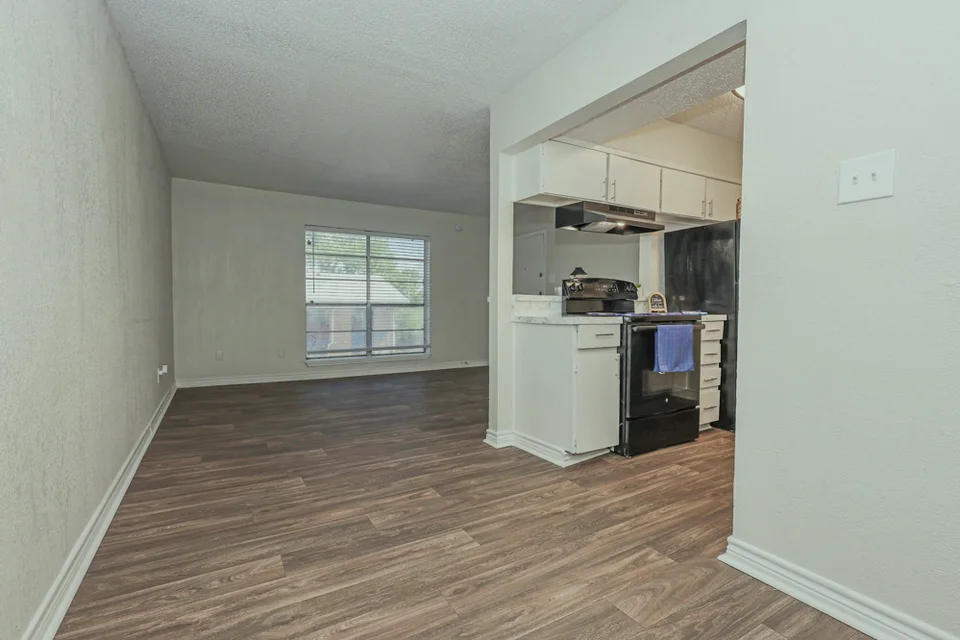 An empty room opening to a kitchen with white cabinets and a black range.