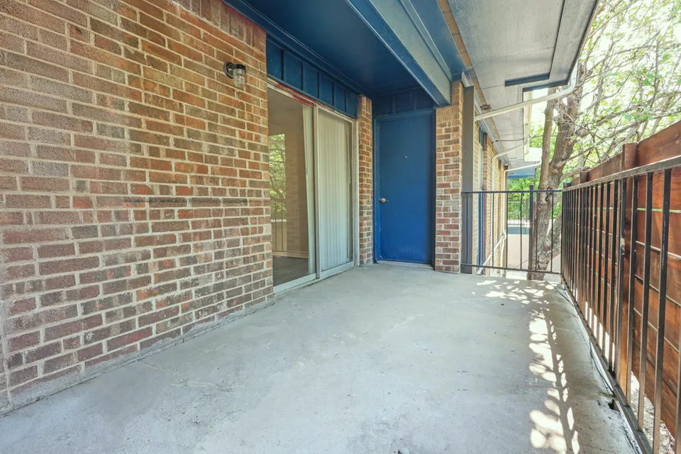 A covered walkway in brick, with an iron rail and a blue apartment door.