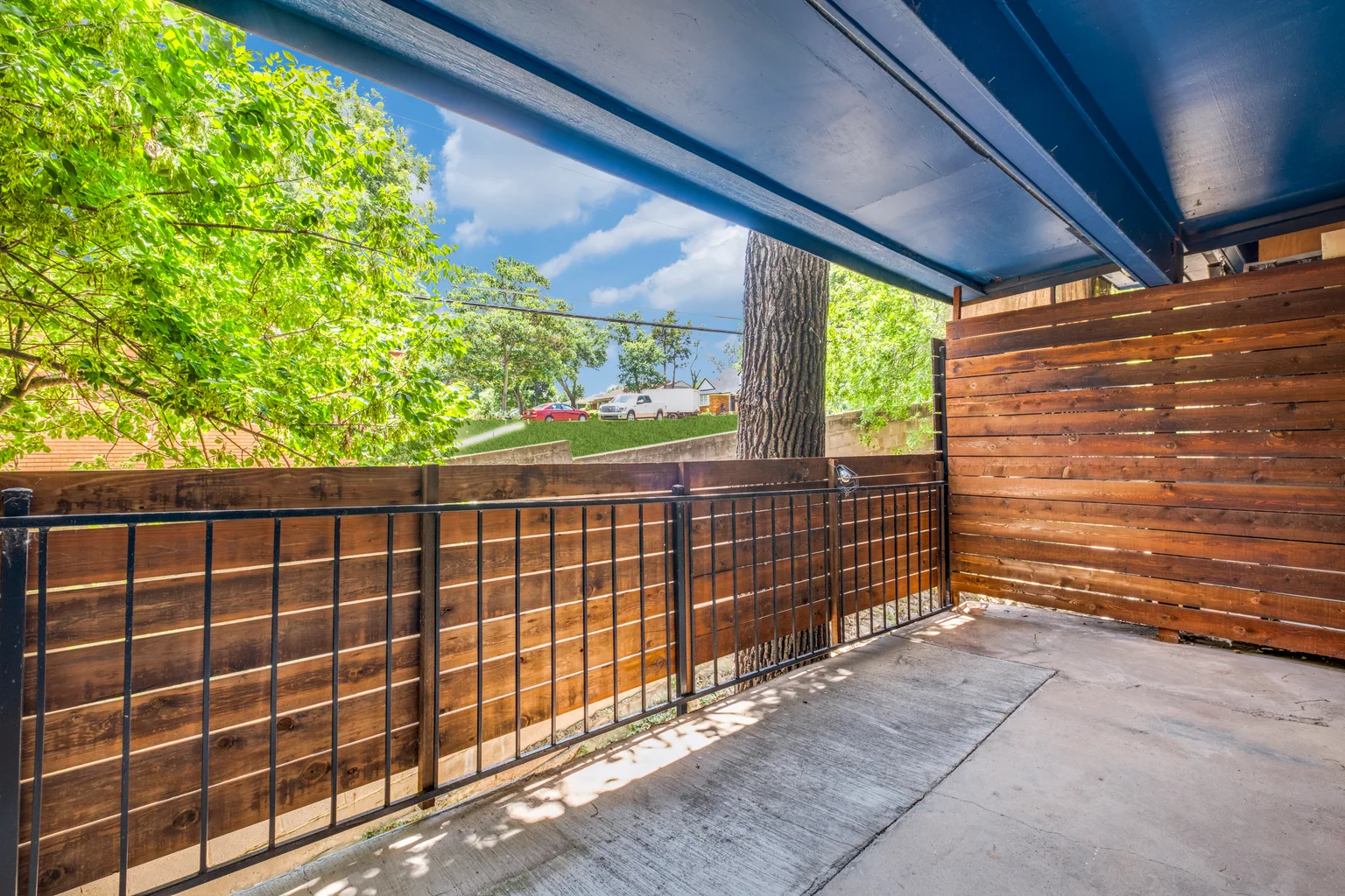 A covered balcony with an iron rail and a wood privacy screen along one side.
