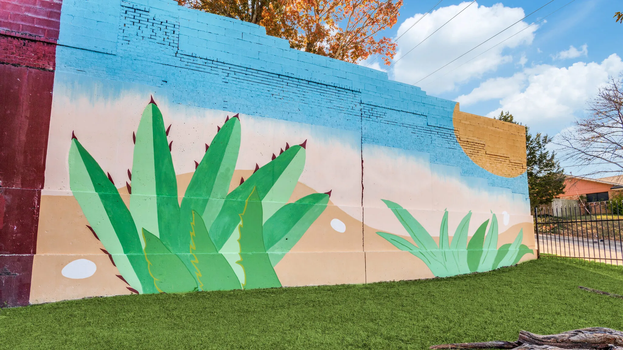 The hand painted mural of green agaves under a gold sun, on the boundary wall above the lawn.