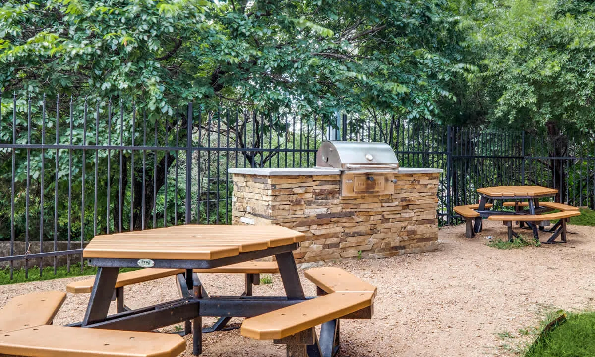 The grill station and wooden picnic tables under the trees.