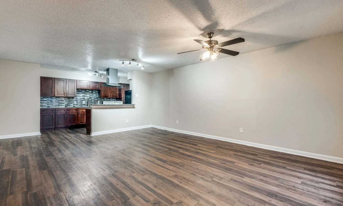 A living room open through to a kitchen with dark cabinets and a glass mosaic backsplash.