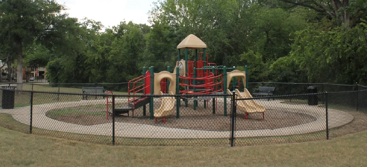 The playground and its safety surround at Briar Gate Park, ringed by trees.