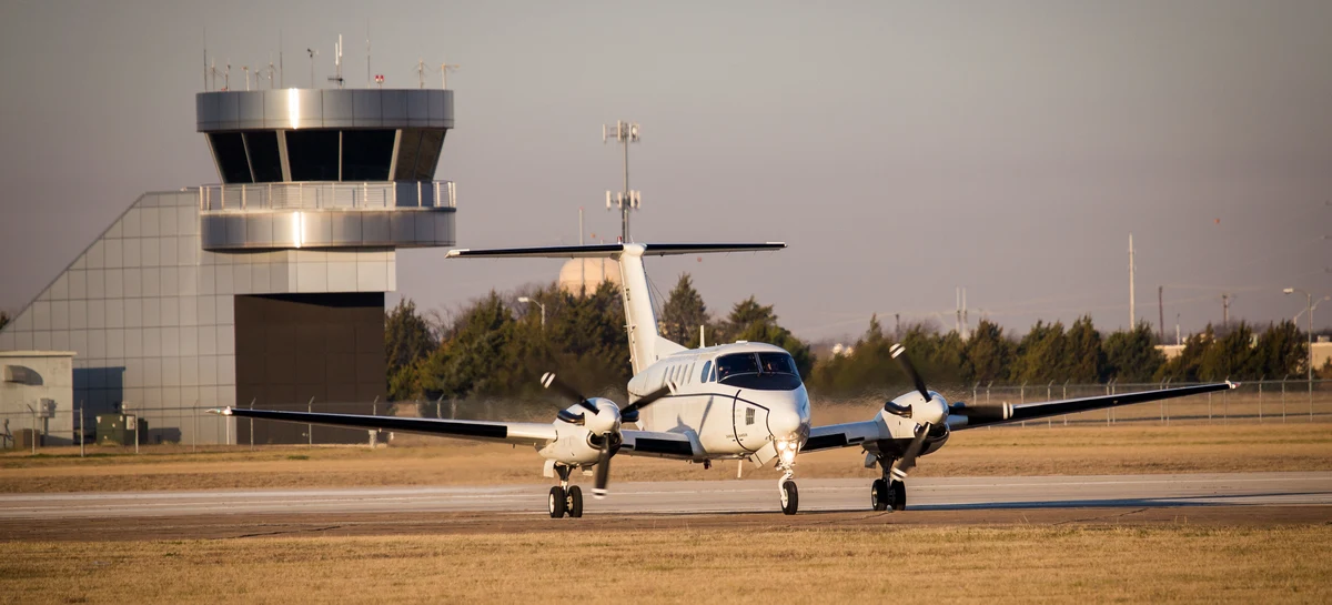 A twin-engine aircraft taxiing past the control tower at Dallas Executive Airport.