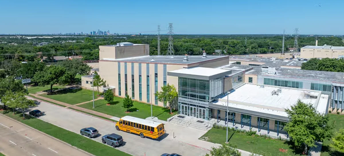 Justin F. Kimball High School from the air, a school bus at the entrance and the Dallas skyline beyond.