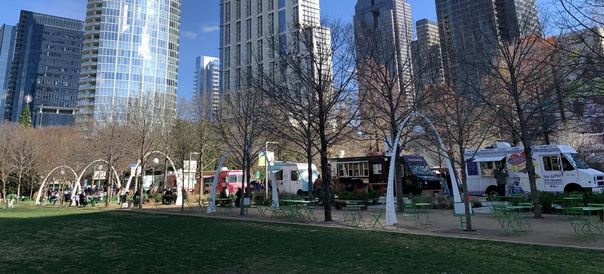Food trucks and white arch sculptures on the lawn at Klyde Warren Park, with the Dallas skyline behind.