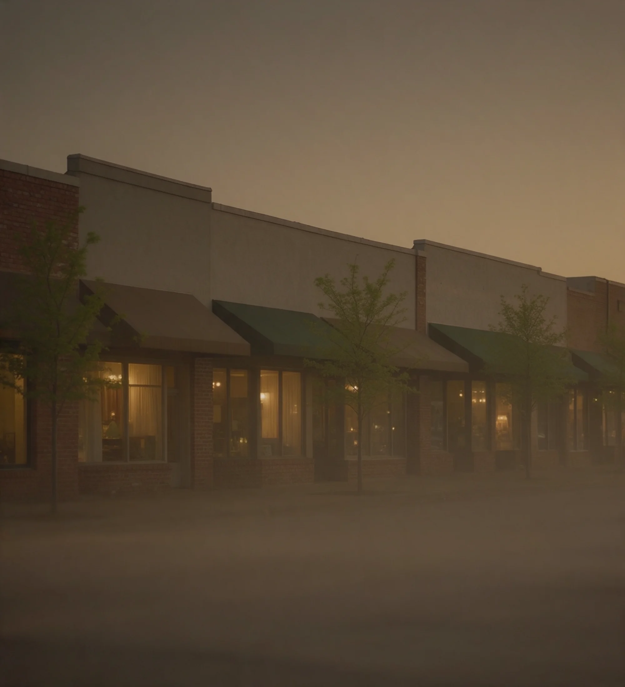 A row of low storefronts at dusk, warm light behind the windows.